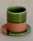 Ceramic cup with green top and terracotta base on a matching saucer against a beige background