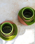 Two green ceramic cups with terracotta bases on a beige surface