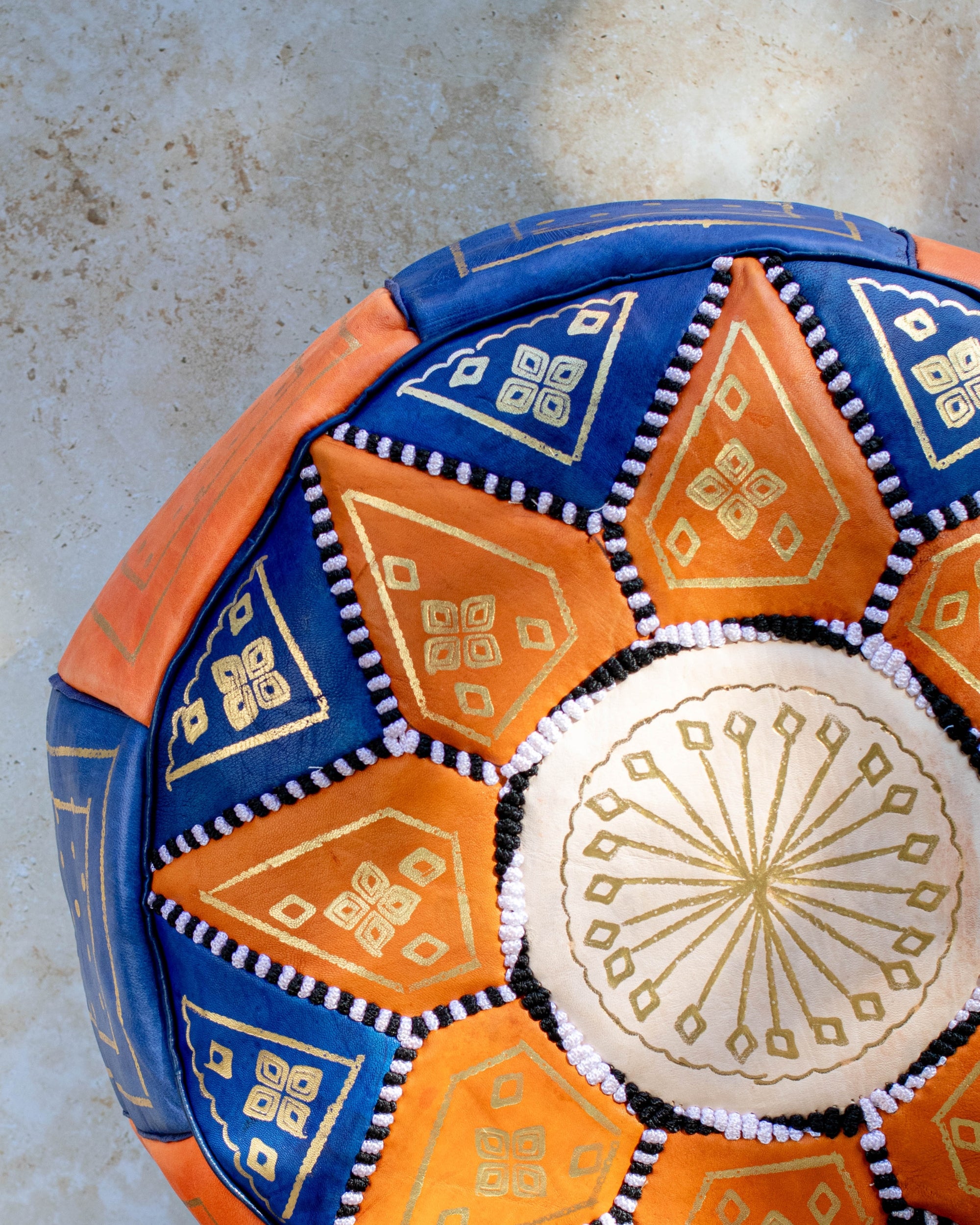 Close up of gold embroidery on blue and orange leather pouf