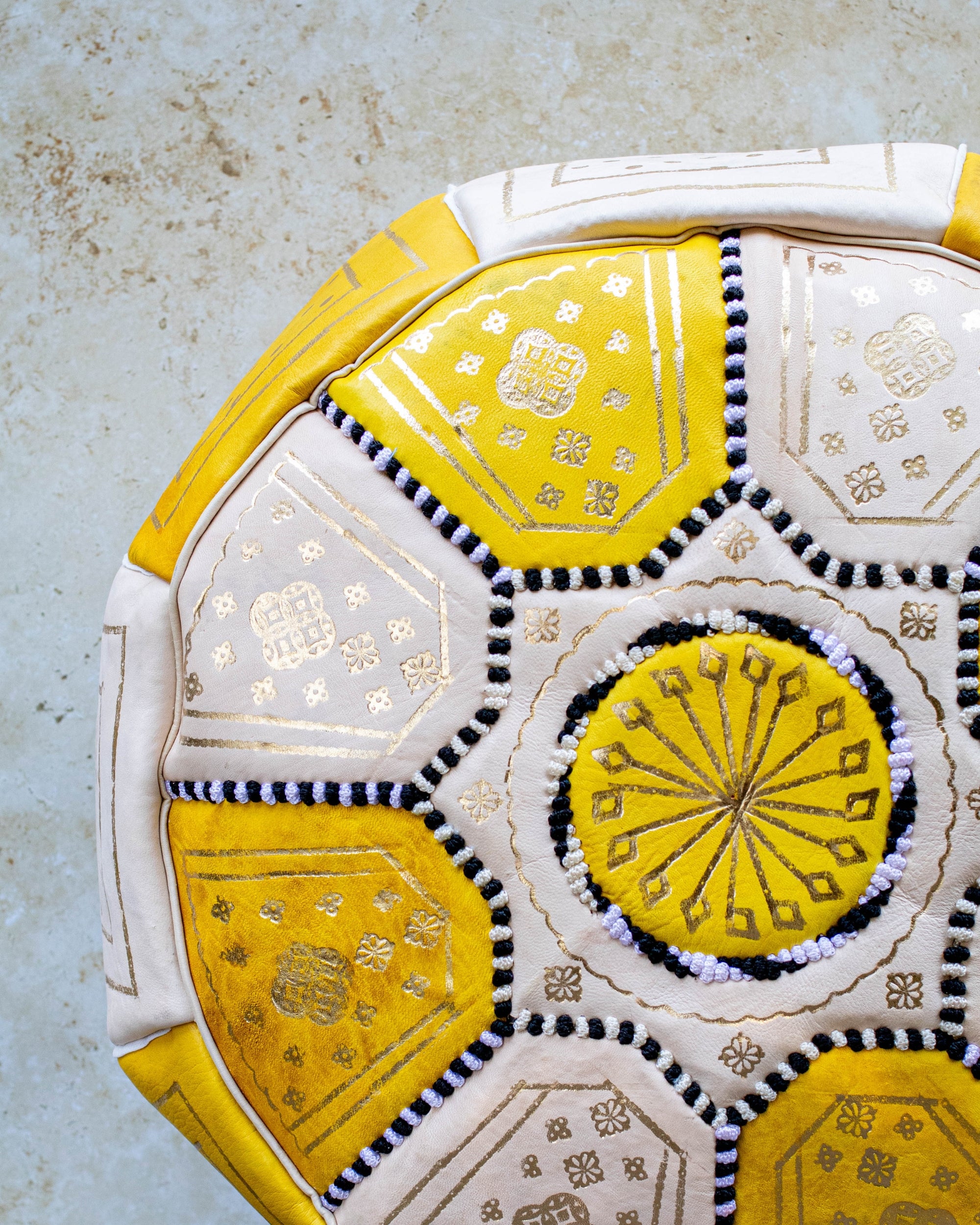 Close up of gold embroidery on yellow and cream leather pouf