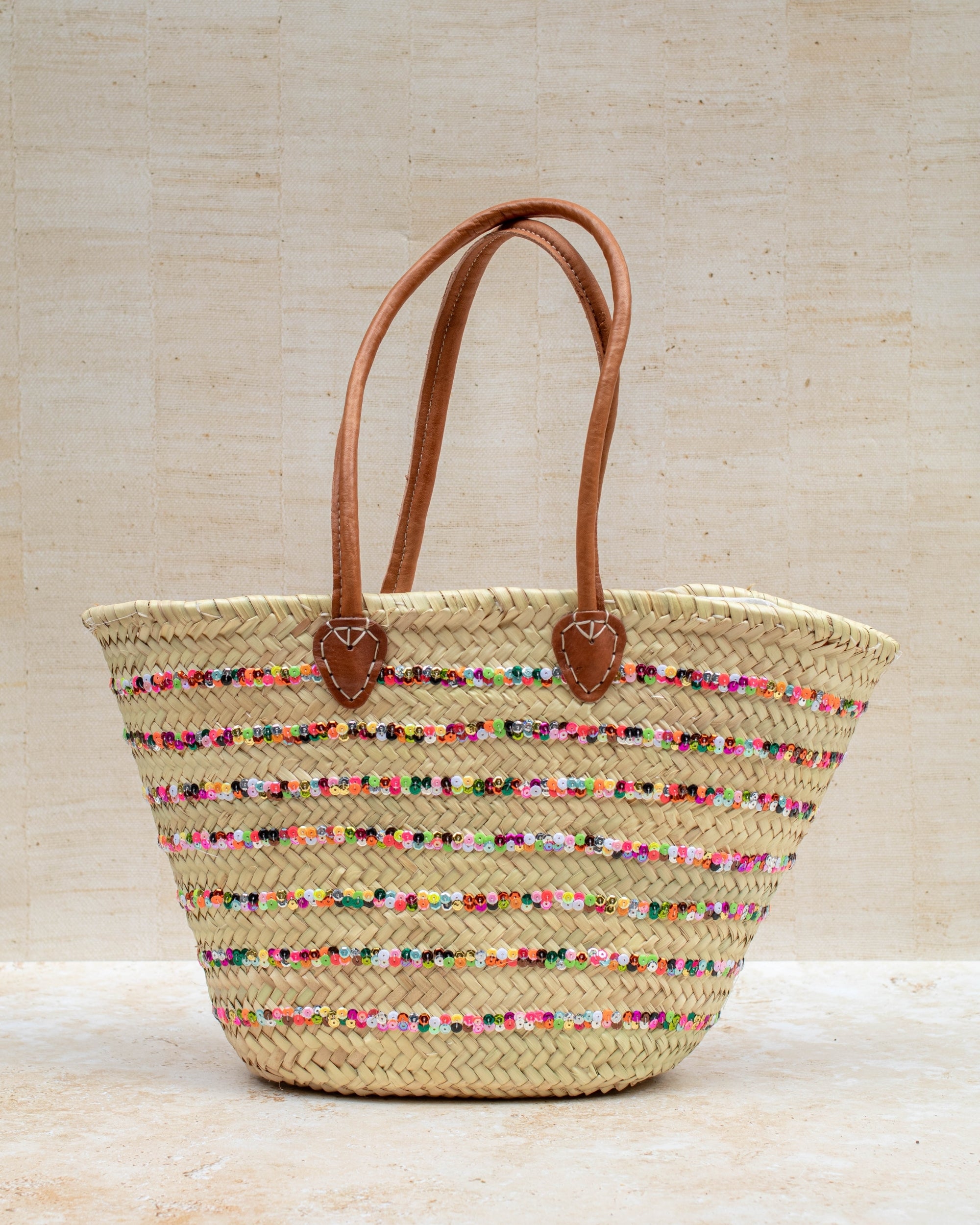 Woven straw bag with colorful accents and brown handles on a light wooden background