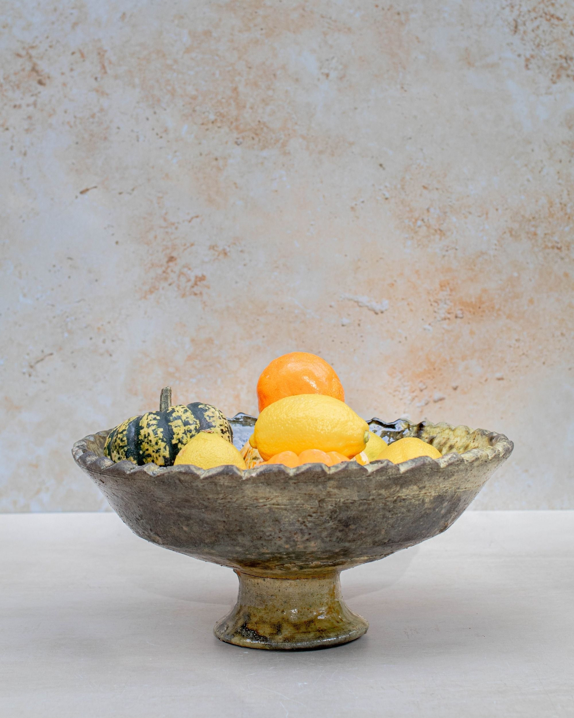 Ochre pedestal bowl filled with lemons on neutral background