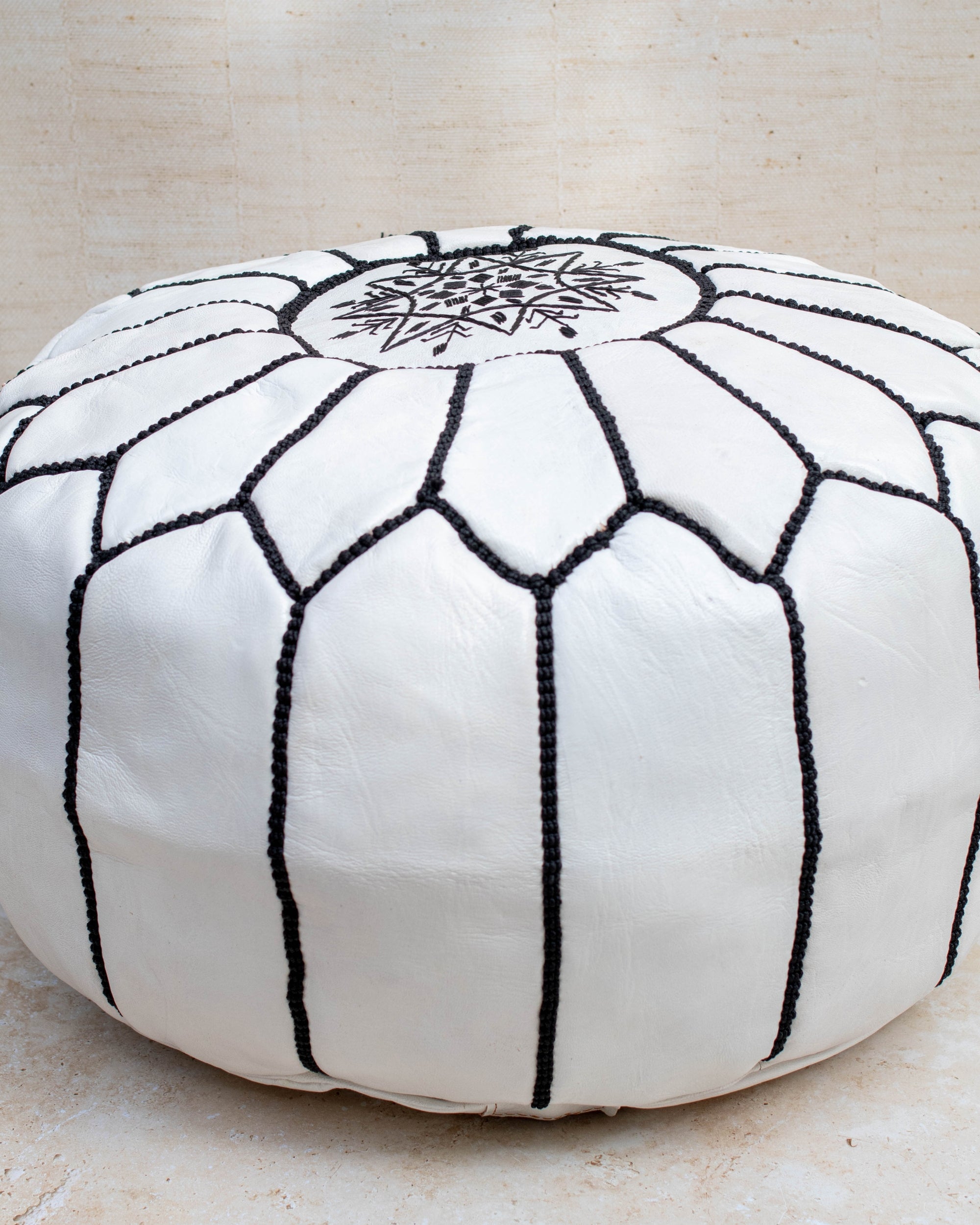White and black stitching pouf styled in living room as ottoman