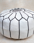 White and black stitching pouf styled in living room as ottoman