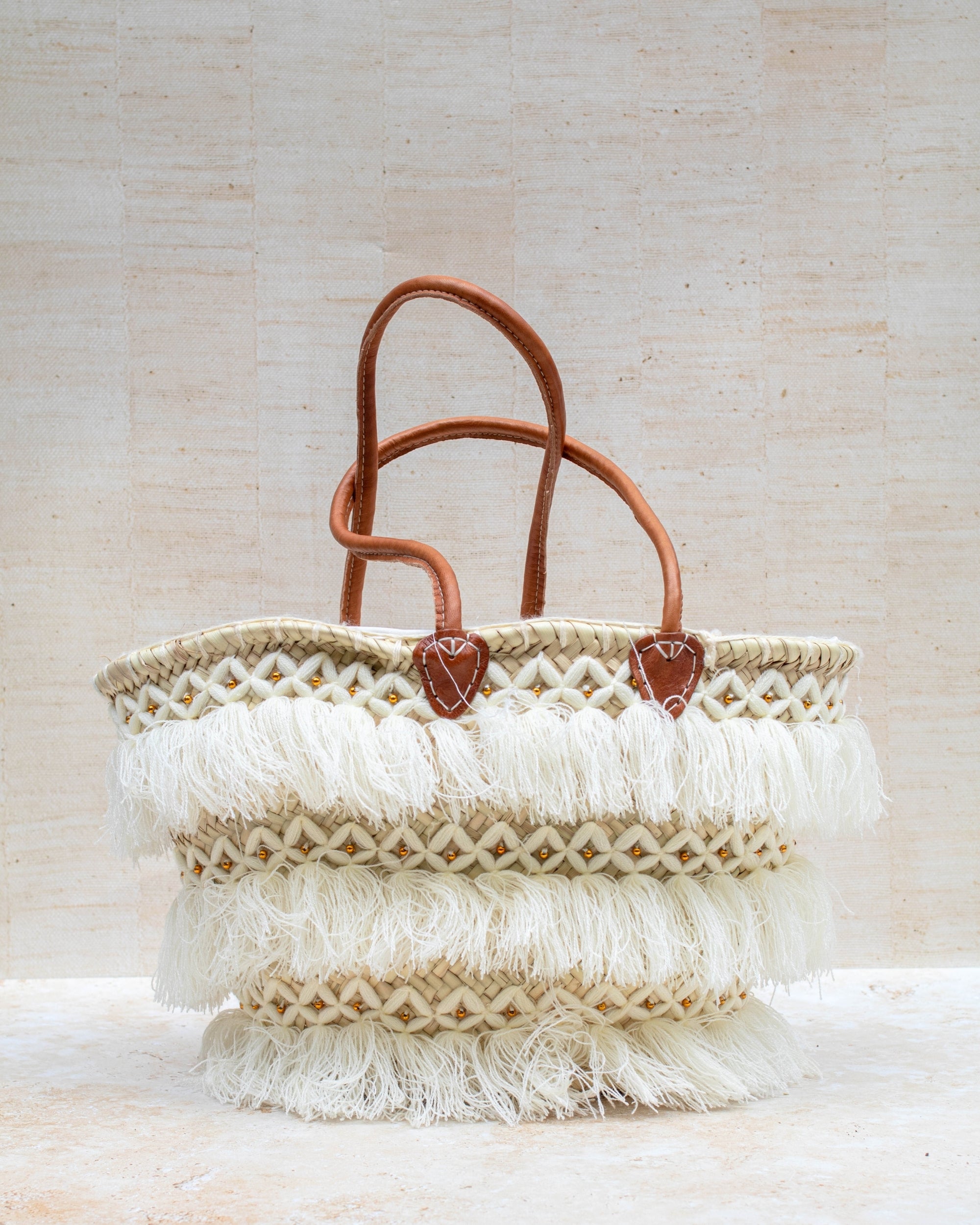 Woven bag with leather handles and tassels on a light background