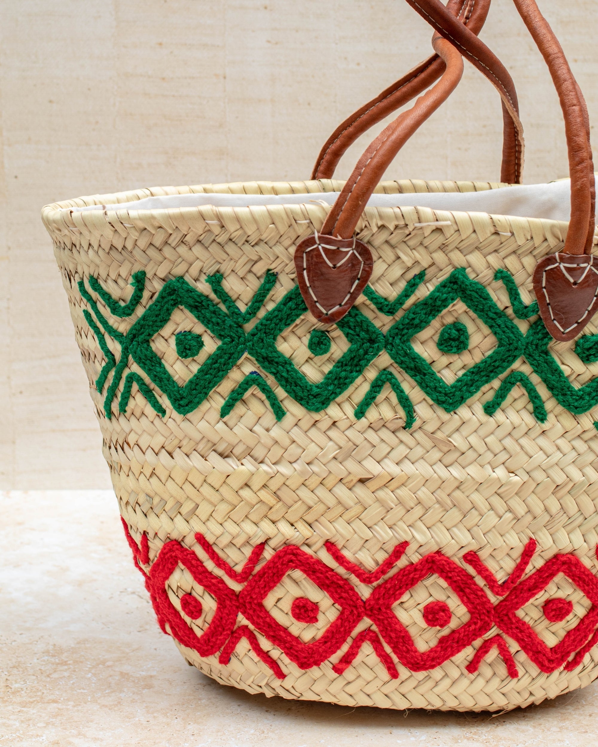 Woven basket with green and red patterns and brown handles on a light background