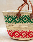 Woven basket with green and red patterns and brown handles on a light background