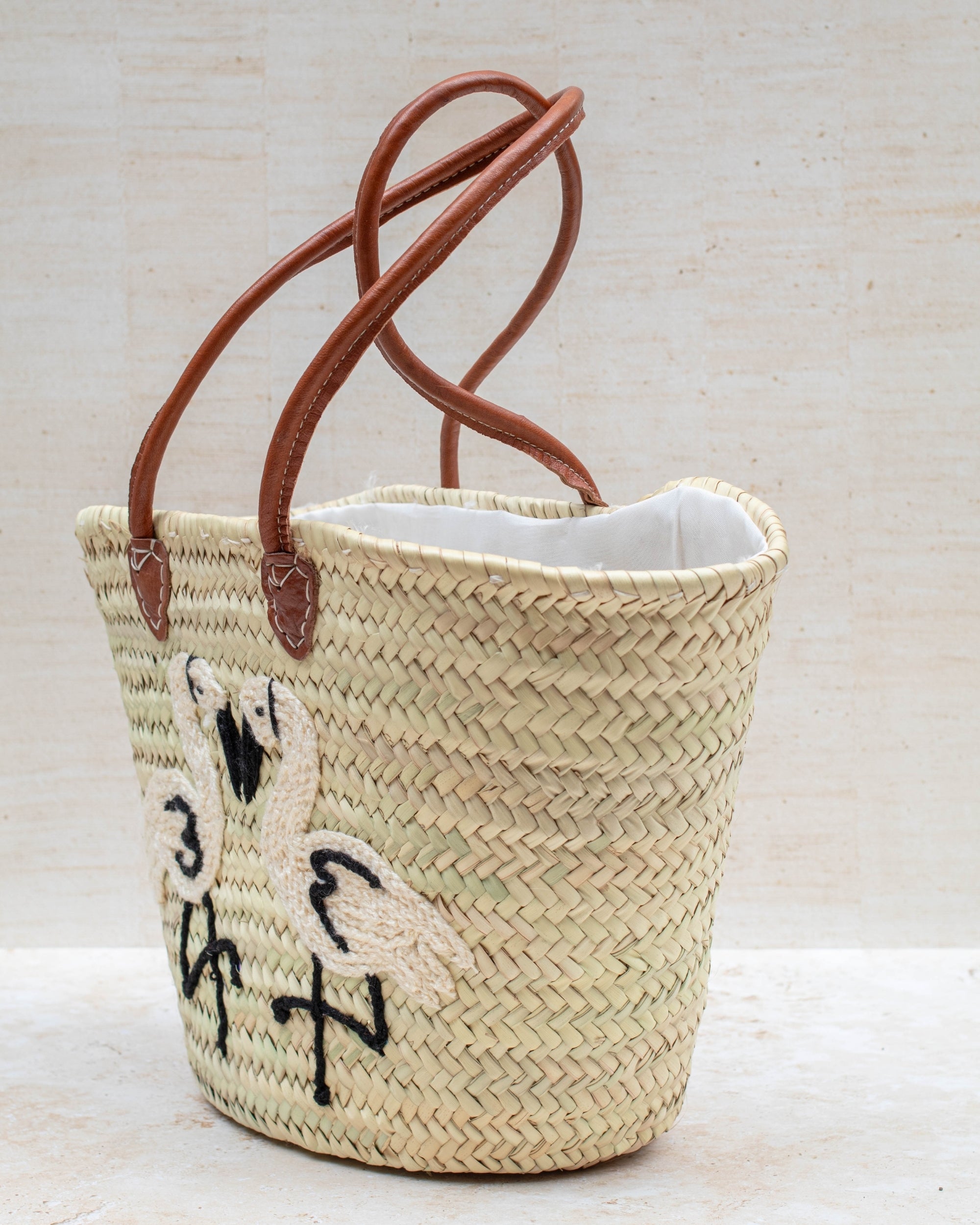 Woven basket with leather handles and embroidered design on a light background