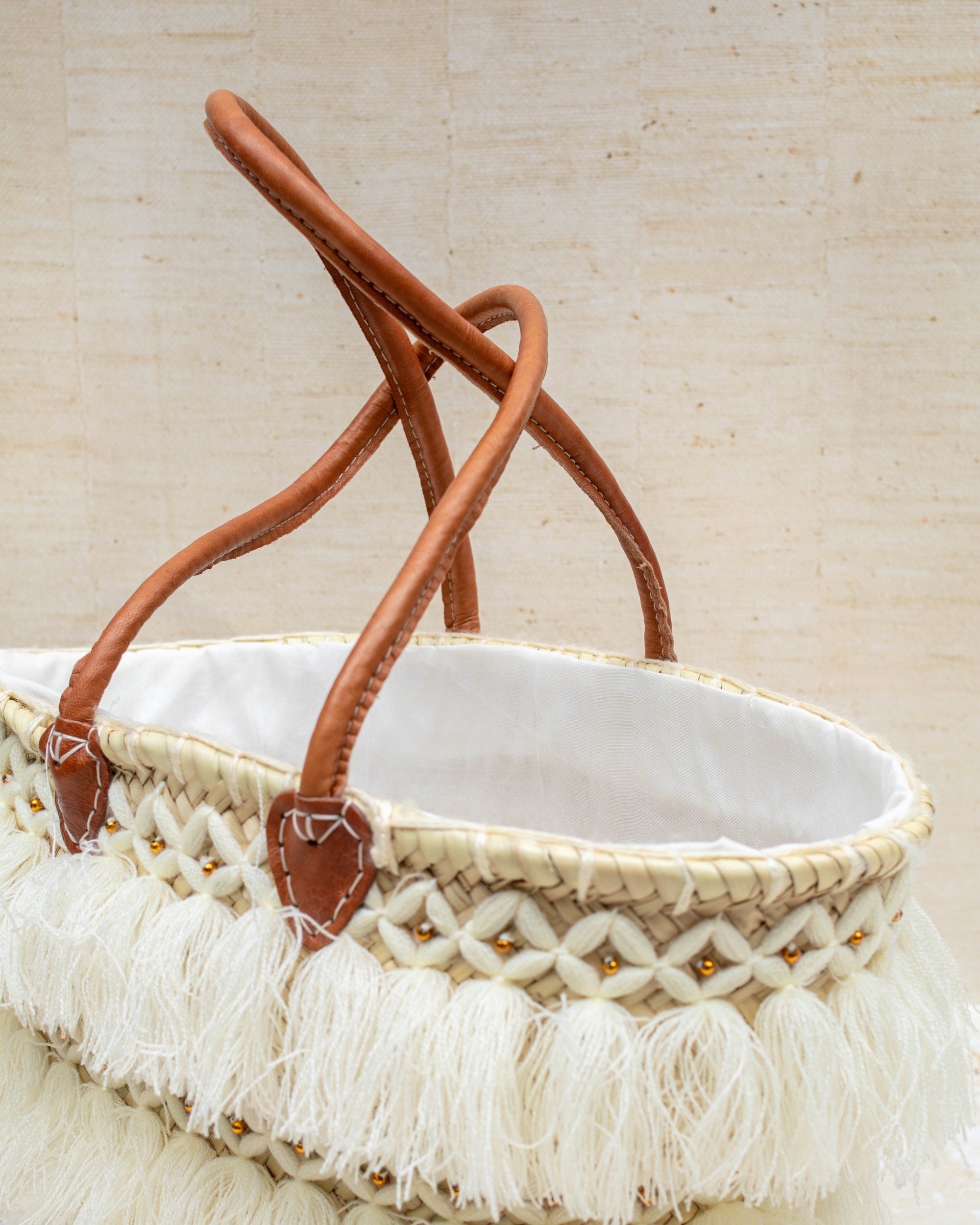 Woven basket with leather handles and white fringe on a beige background