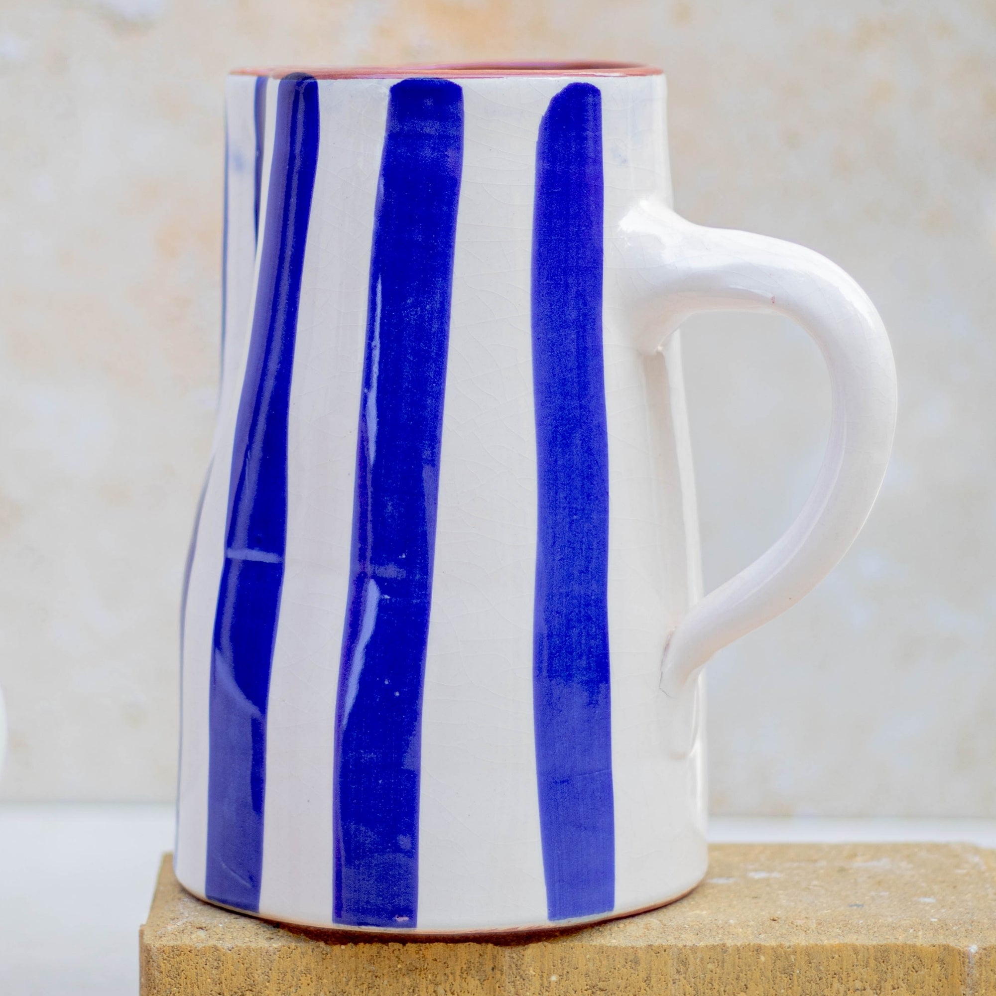 White mug with blue vertical stripes on a wooden block against a beige background