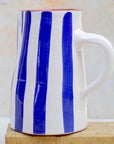 White mug with blue vertical stripes on a wooden block against a beige background