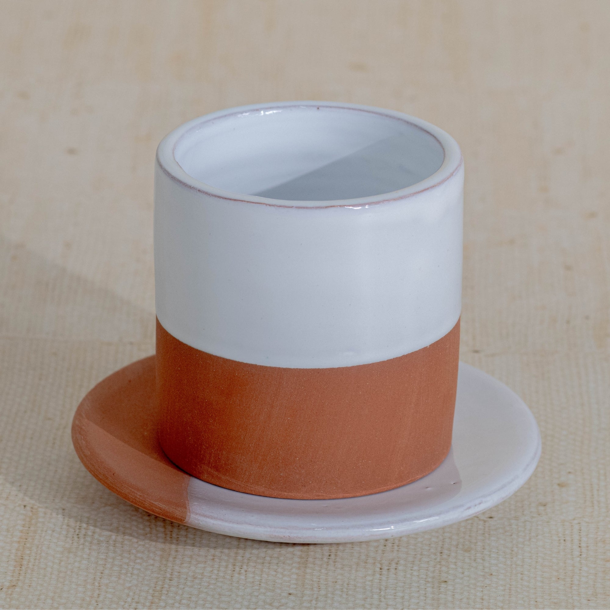 Ceramic cup with a white top and terracotta bottom on a beige background