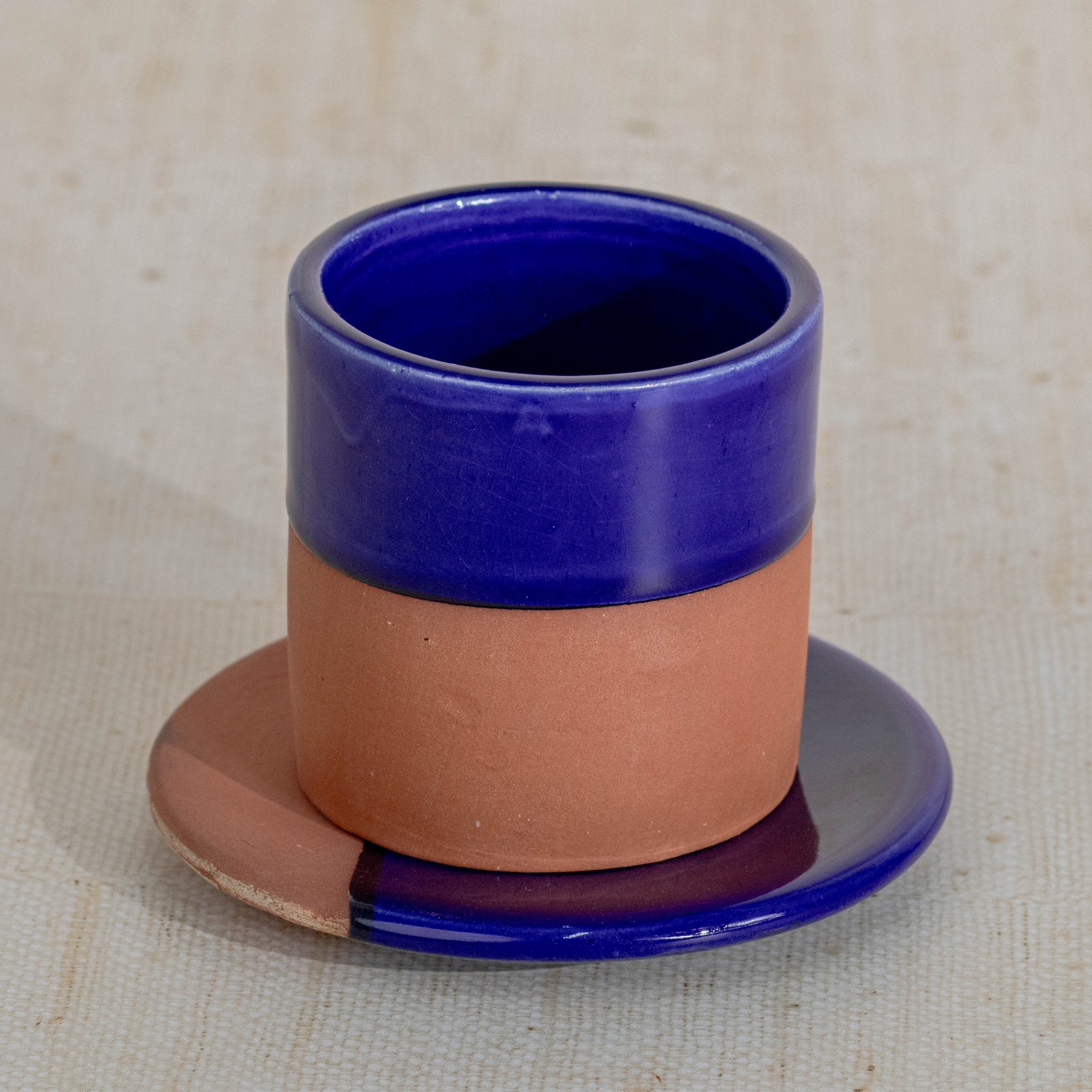 Ceramic cup with blue top and brown bottom on a matching saucer against a beige background