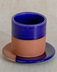 Ceramic cup with blue top and brown bottom on a matching saucer against a beige background