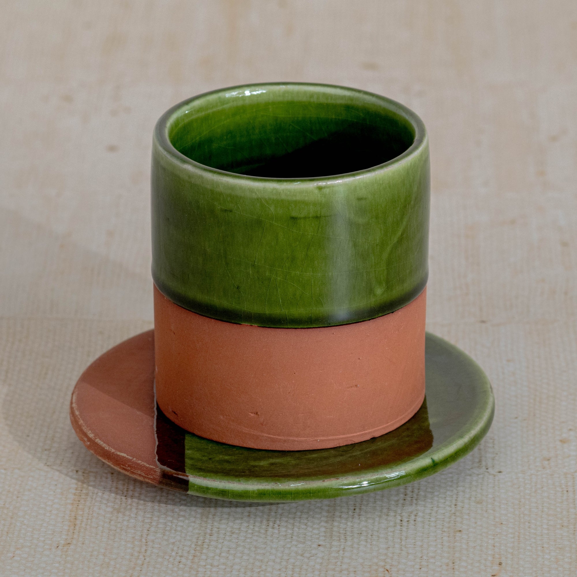 Ceramic cup with green top and terracotta base on a matching saucer against a beige background