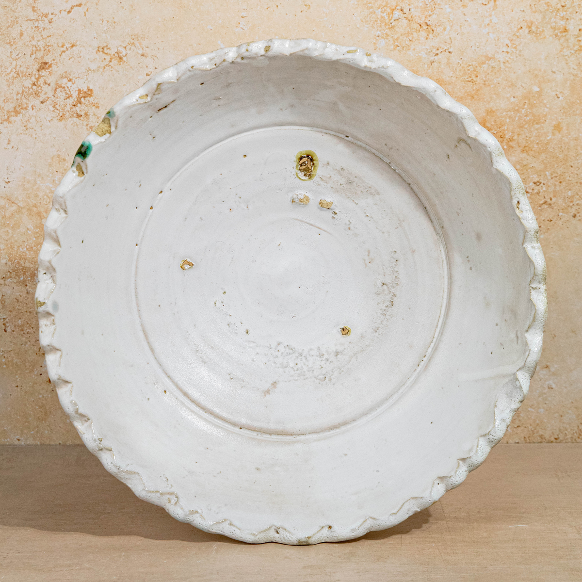 A large white ceramic bowl with a scalloped rim, photographed from directly above on a light wood surface against a textured beige background.
