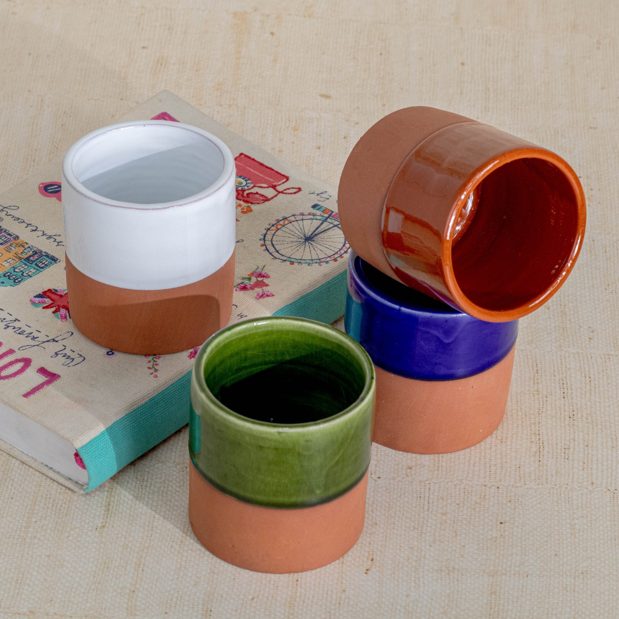 Set of colorful ceramic pots on a textured surface with books underneath.