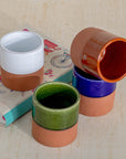 Set of colorful ceramic pots on a textured surface with books underneath.