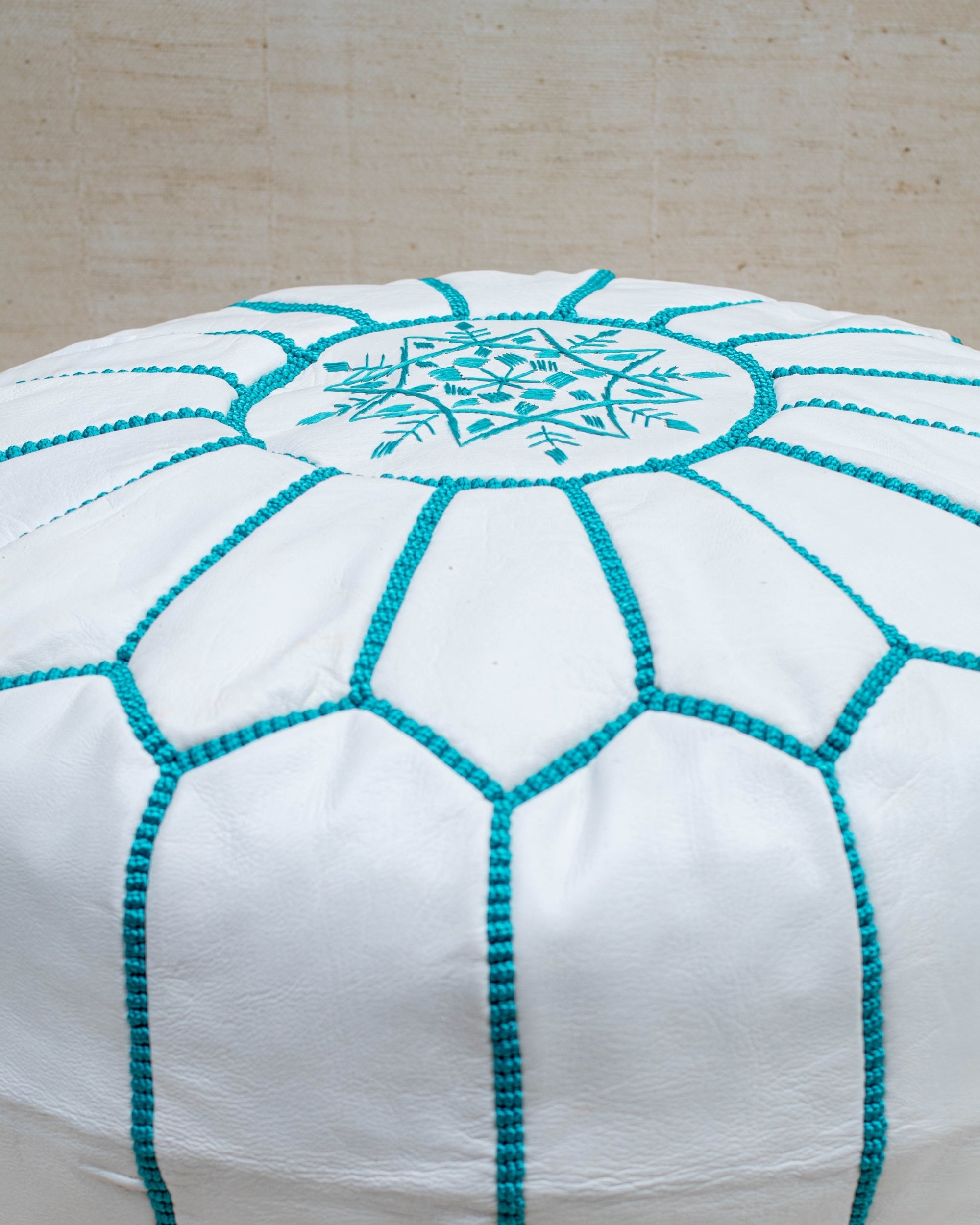 White and turquoise pouf styled in living room as ottoman
