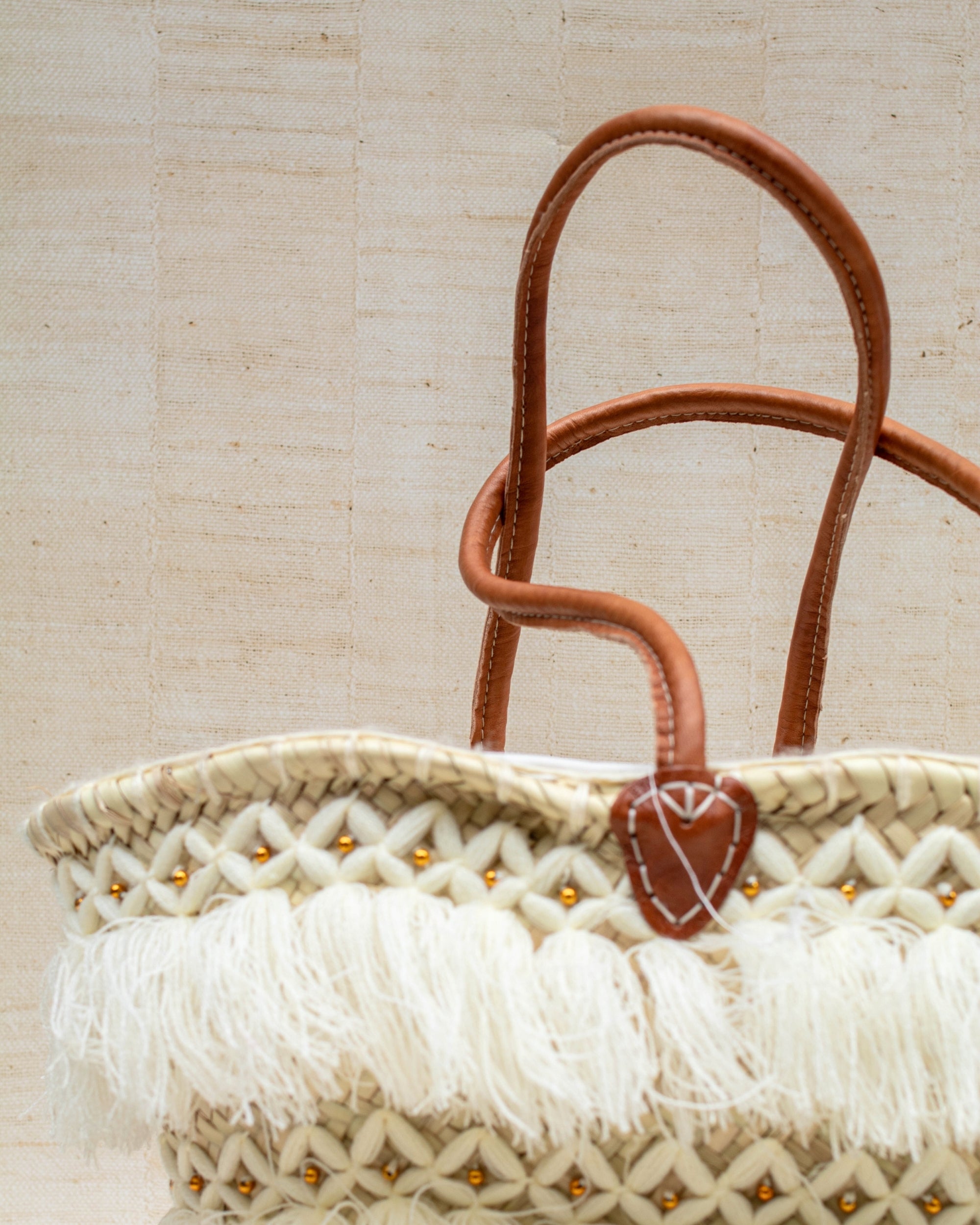 Woven bag with leather handles and tassels on a beige background